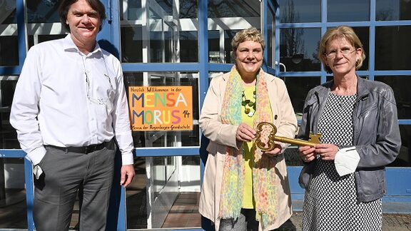 Das Bild zeigt Geschäftsführer der STADT UND LAND Ingo Malter, Bildungsstadträtin Korte und  Schulleiterin Dr. Angela Kuttner vor der neuen Mensa